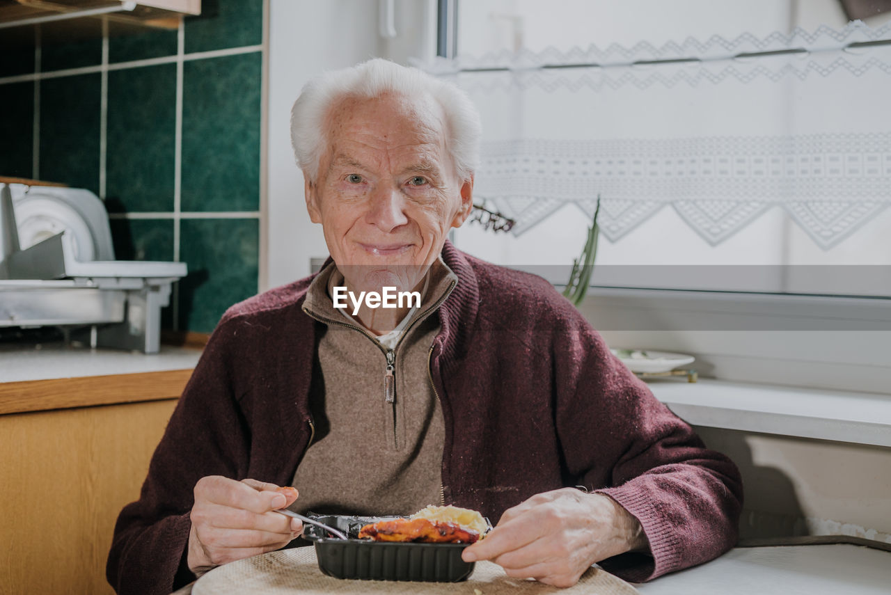 Portrait of smiling senior man eating food at home