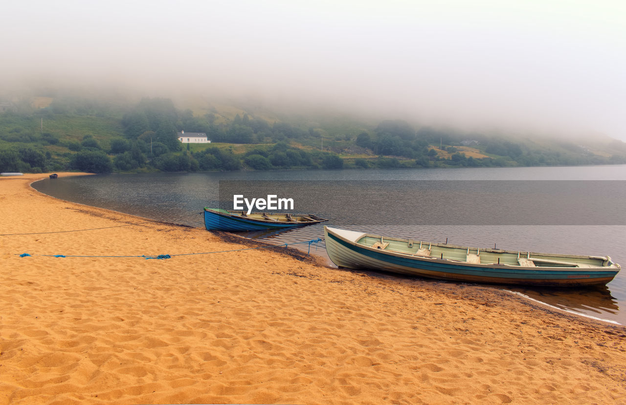 Foggy morning landscape scenery with old wooden fishing boat on sandy beach of loch na fooey 