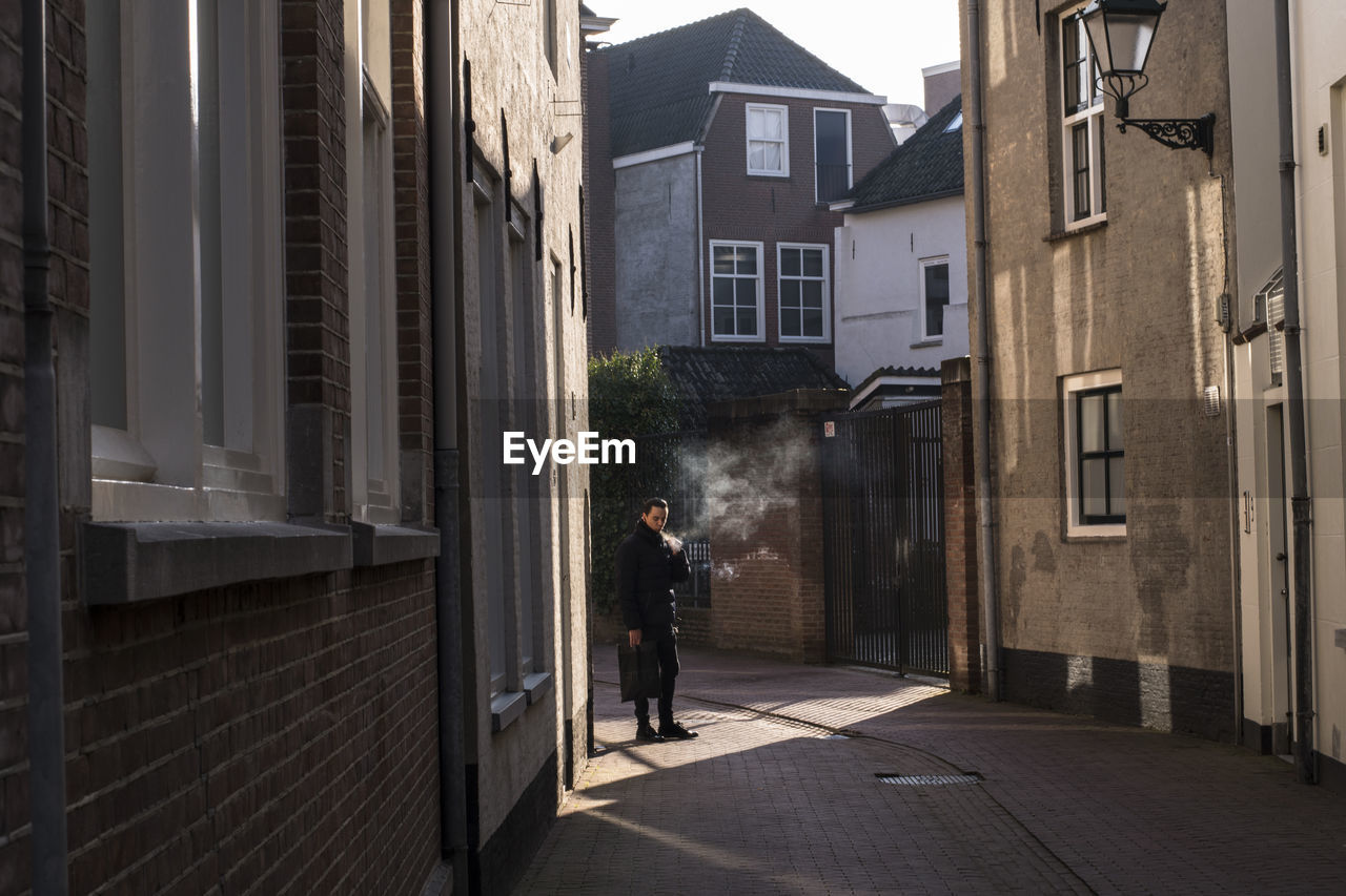 REAR VIEW OF MAN WALKING ON FOOTPATH AMIDST BUILDINGS