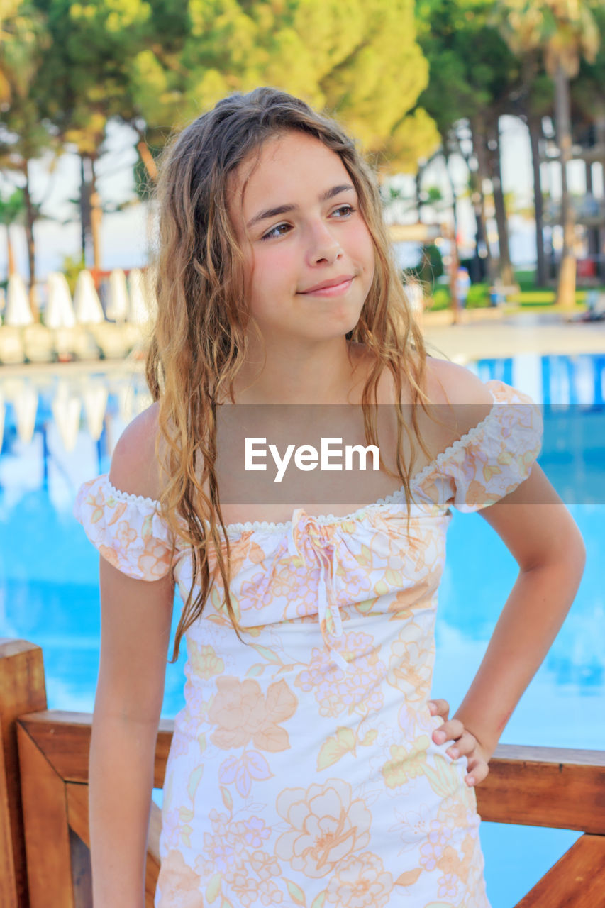 Cute girl looking away while standing by swimming pool