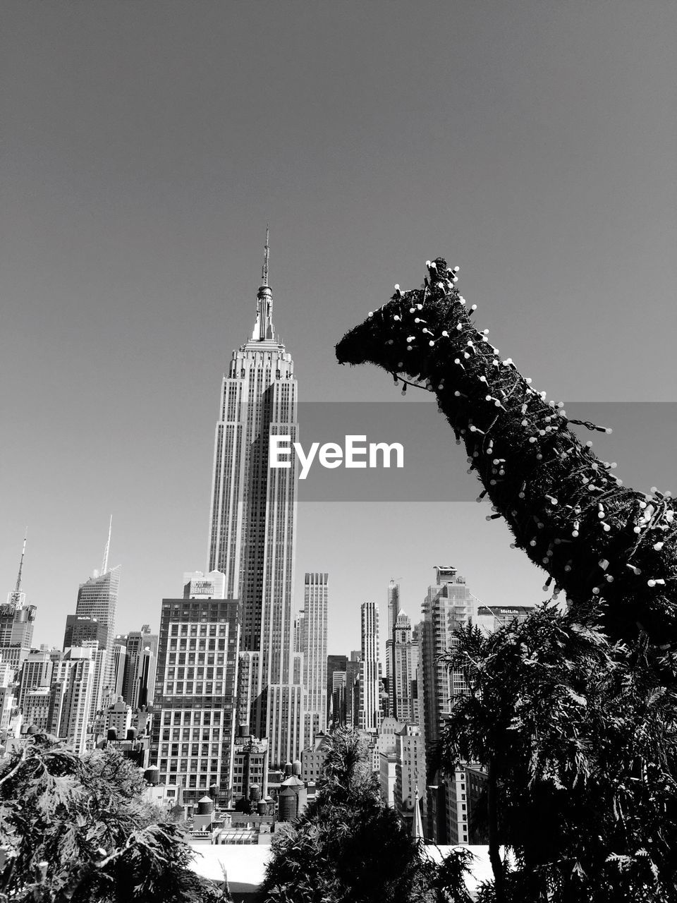 Artificial giraffe with empire state building against clear sky