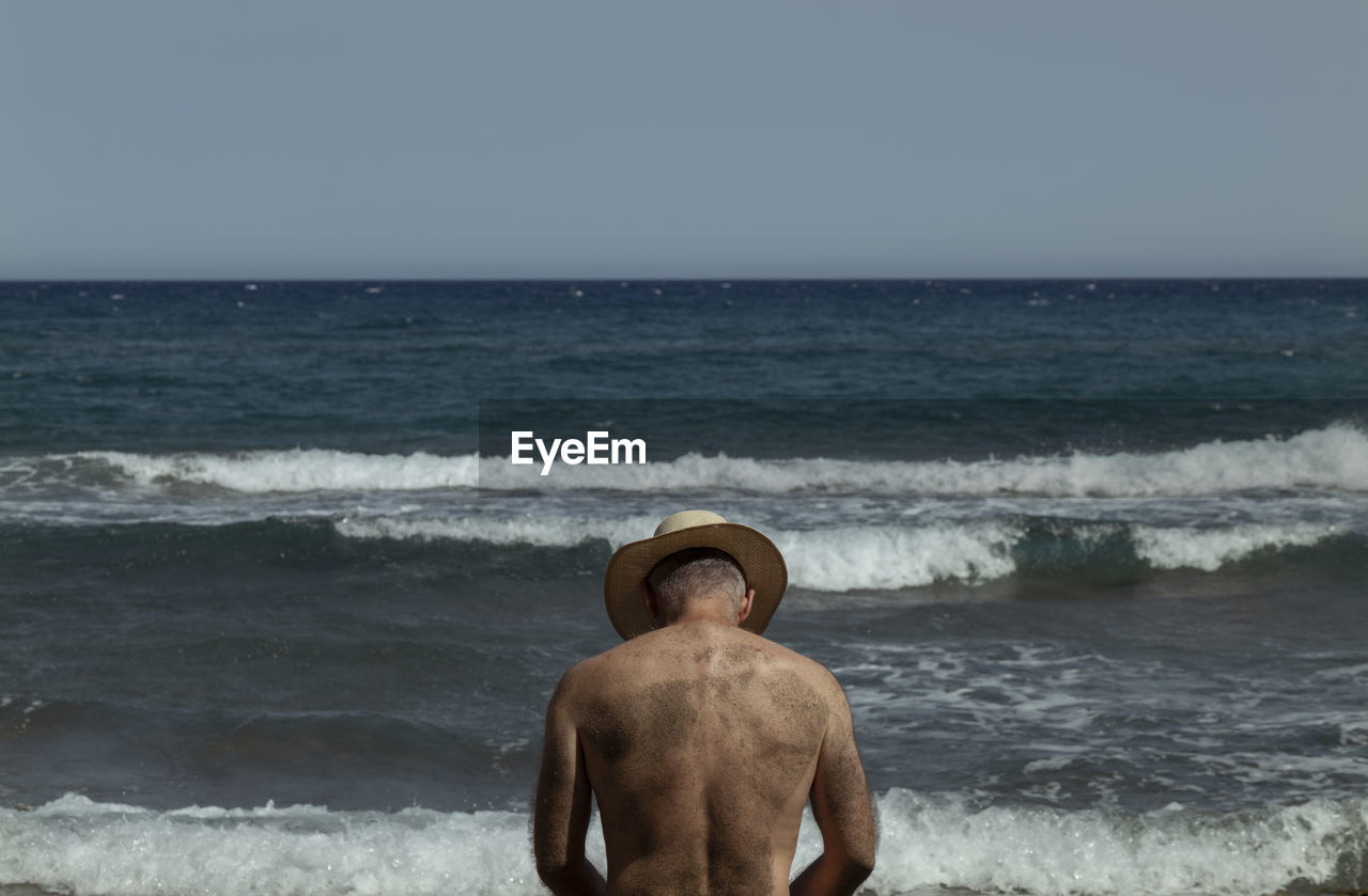 Rear view of shirtless man in hat against sea and sky