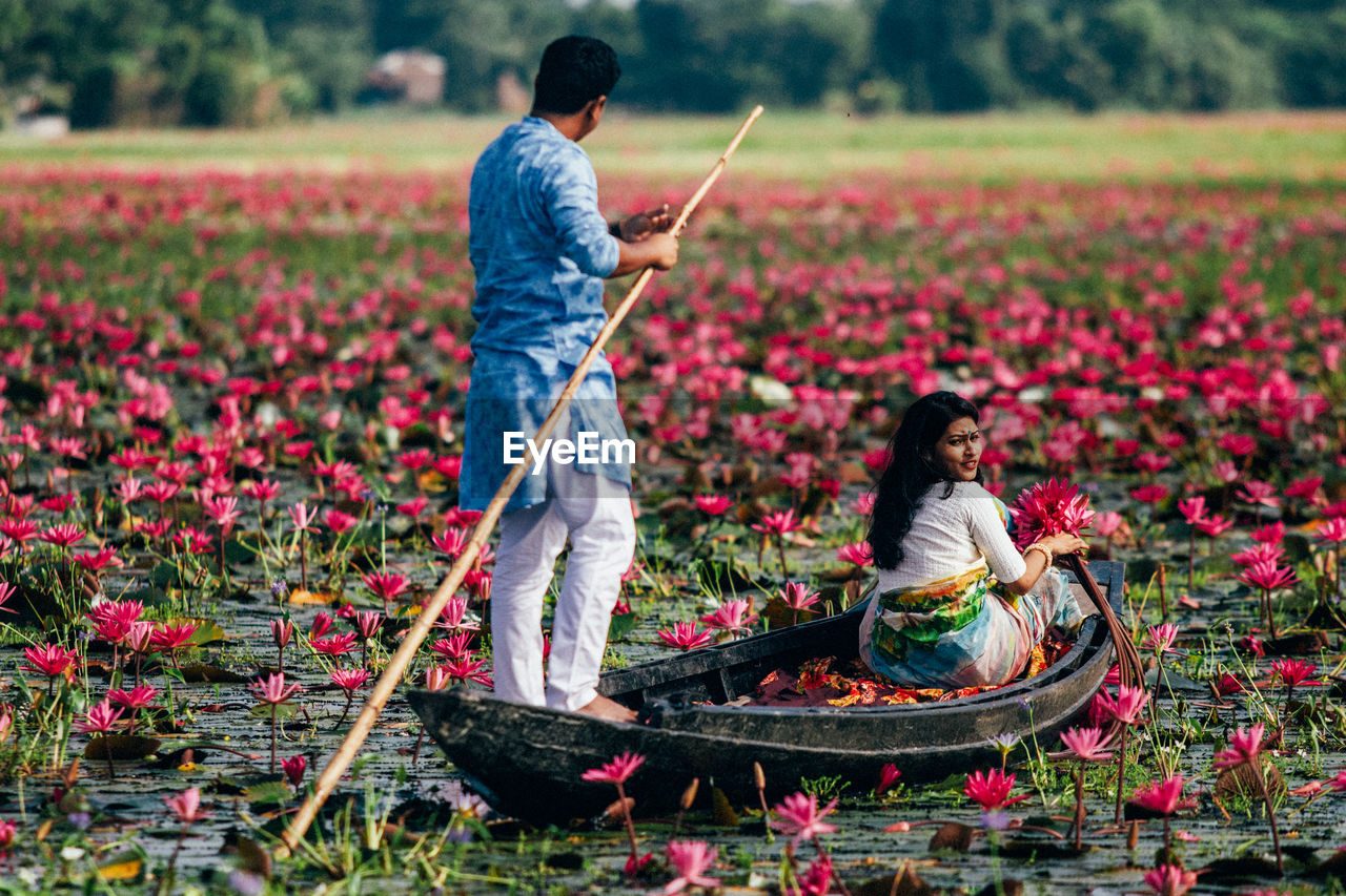 Rear view of man with arms outstretched standing on waterlily pond