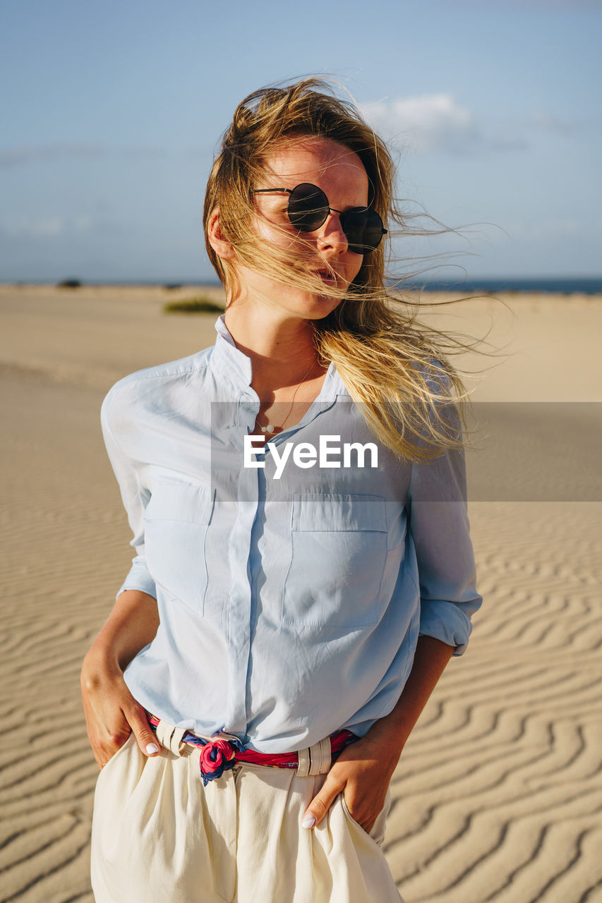 Young woman looking away while standing on sand at desert against sky