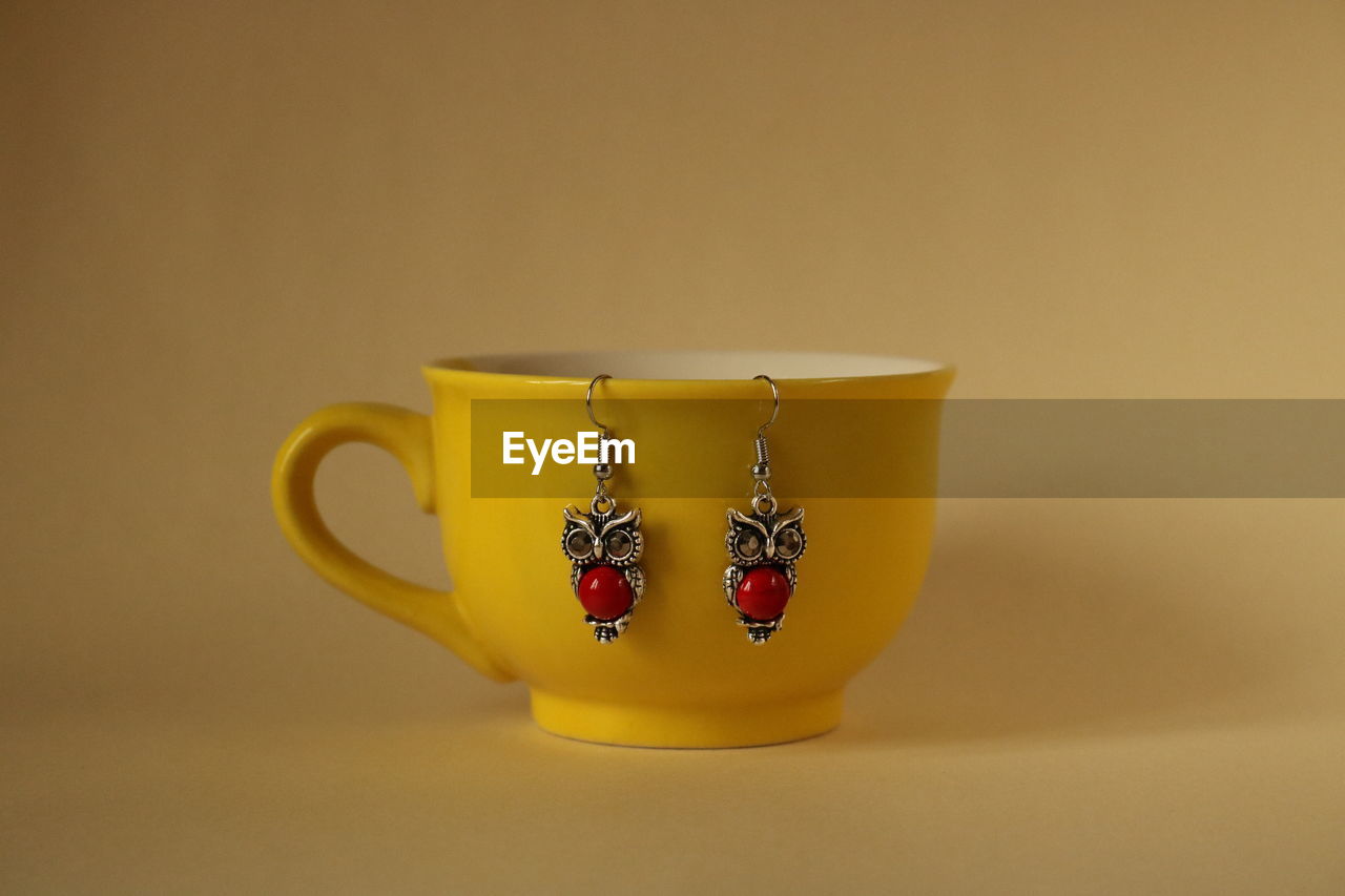 Close-up of earrings with cup over yellow background