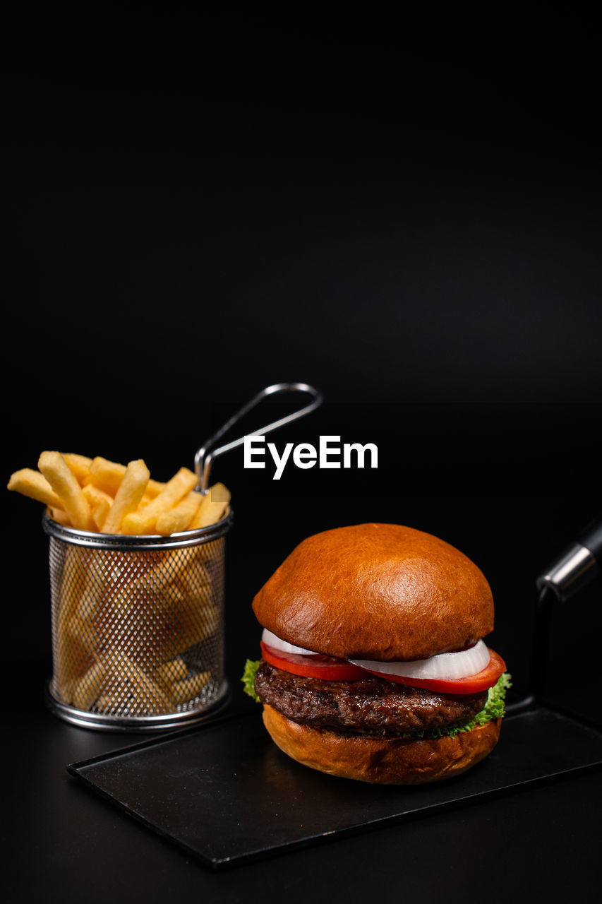Close-up of a burger and fries on table against a black background 