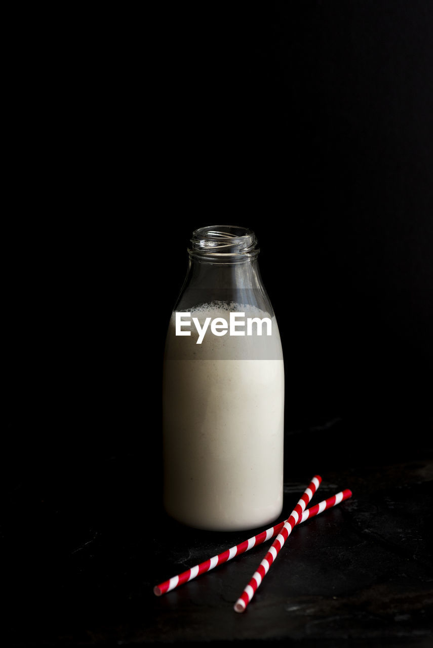 Milk bottle with drinking straws against black background