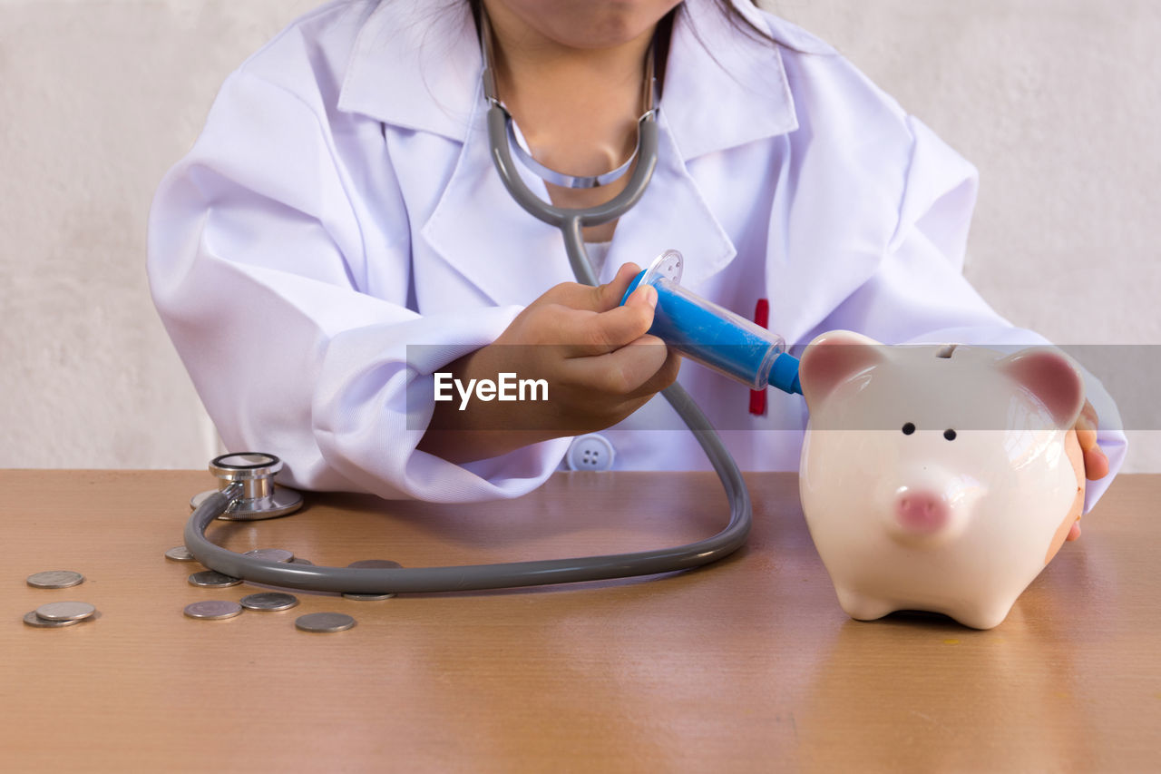Midsection of doctor injecting piggy bank on table