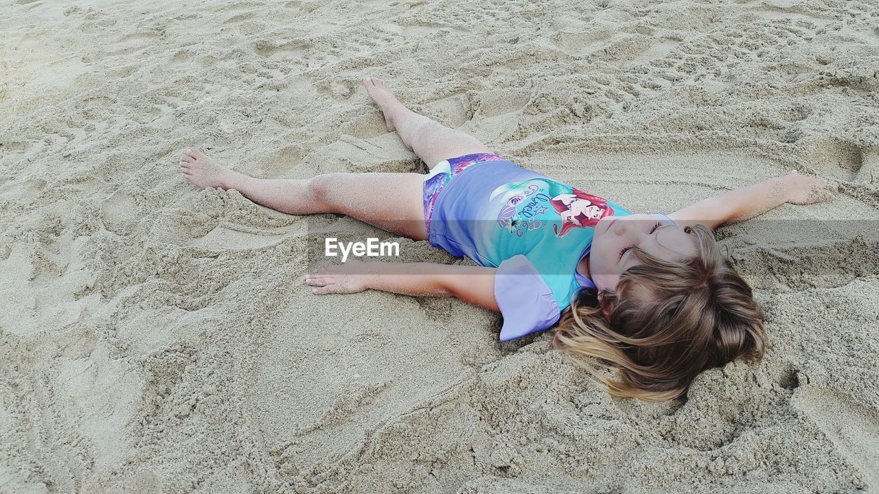 real people, leisure activity, childhood, one person, sand, full length, lifestyles, lying on back, lying down, high angle view, girls, day, beach, elementary age, outdoors, smiling, nature