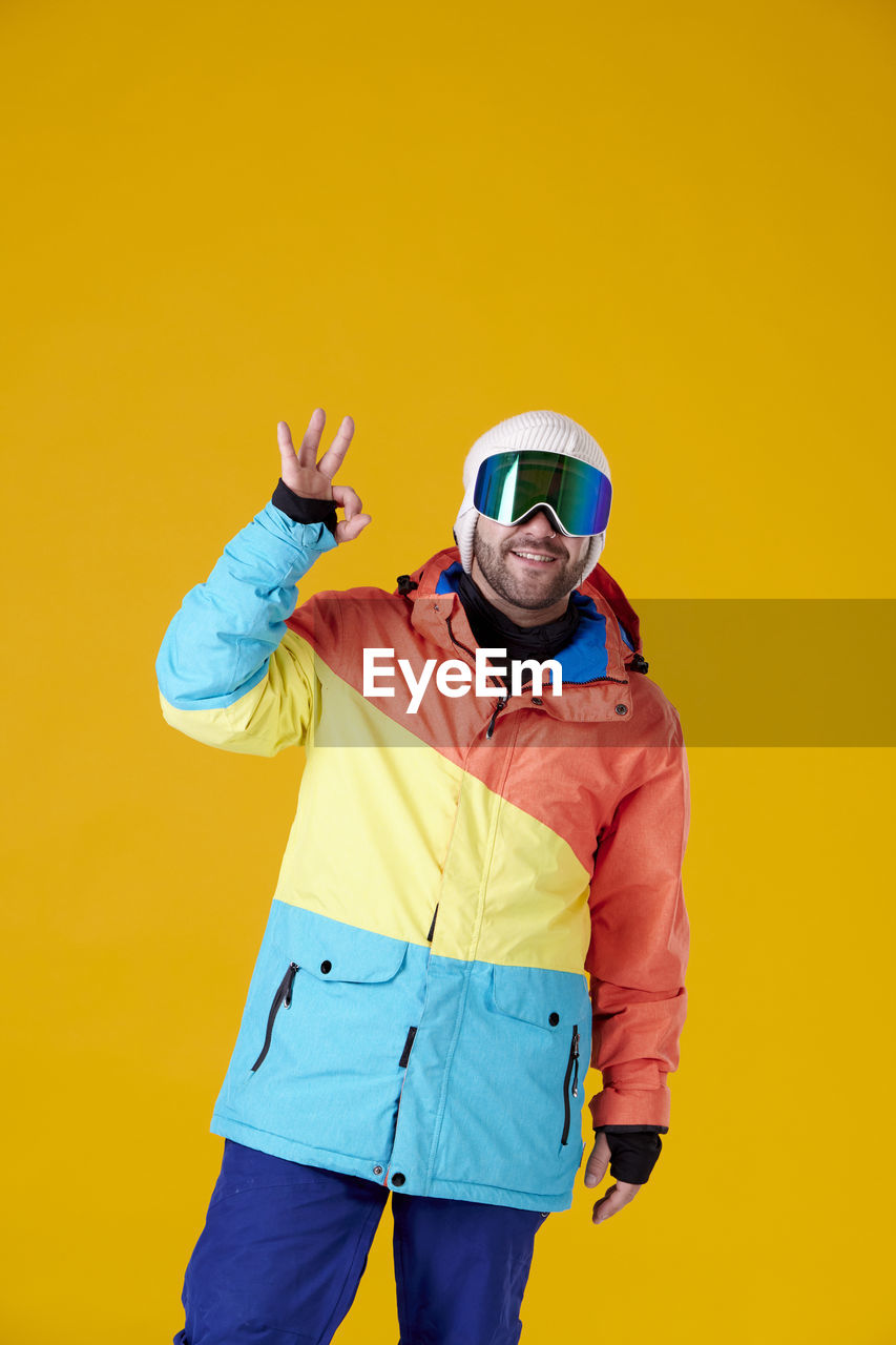 yellow, one person, colored background, yellow background, adult, studio shot, men, clothing, portrait, sports, standing, fun, emotion, indoors, young adult, hood, three quarter length, happiness, copy space, sunglasses, fashion, lifestyles, vibrant color, smiling, looking at camera, sports clothing, person