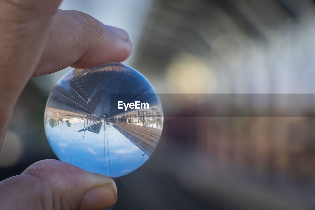 close-up of hand holding crystal ball against sky