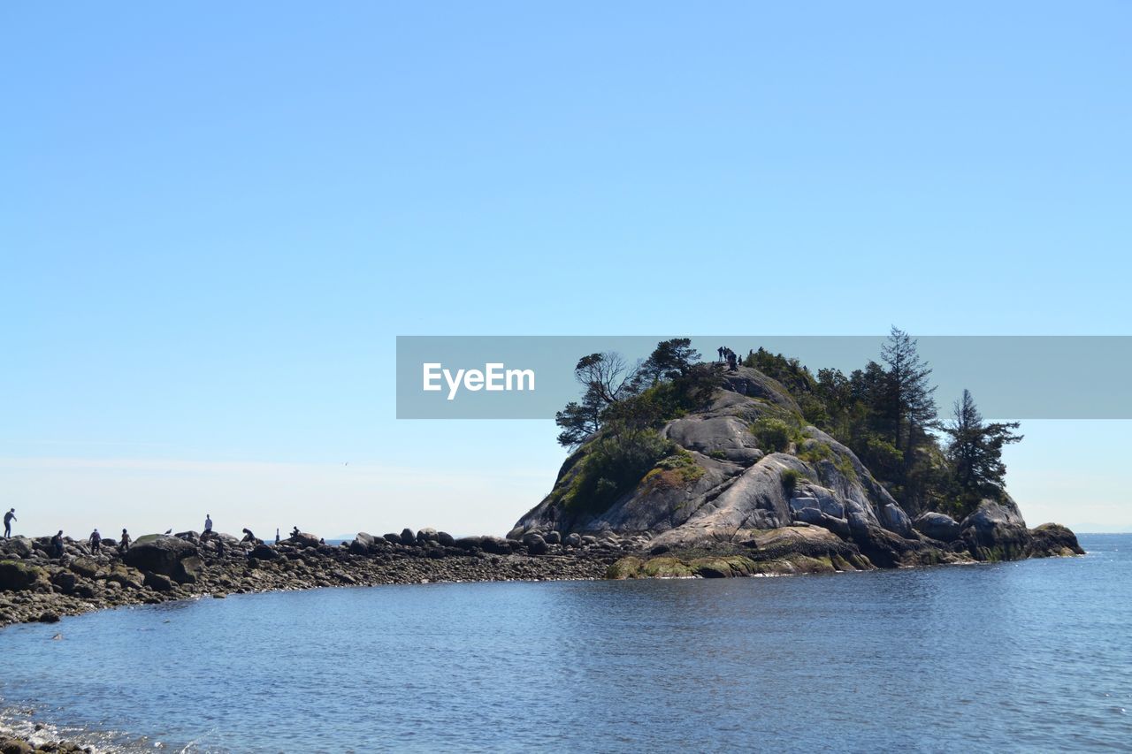 Rock formation in sea against clear blue sky