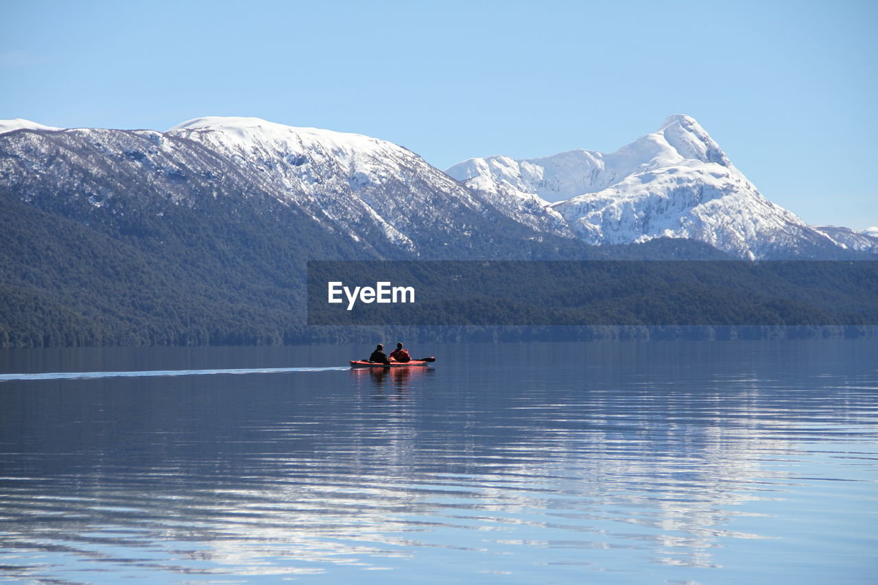 People kayaking on lake against mountains