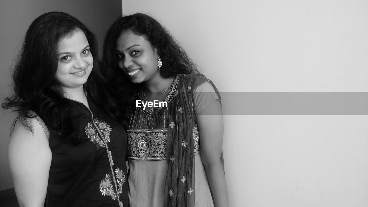 Portrait of smiling friends wearing dress while standing against wall