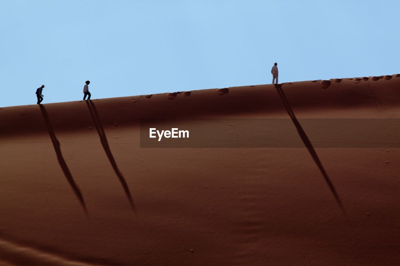 Low angle view of people walking in desert against sky on sunny day