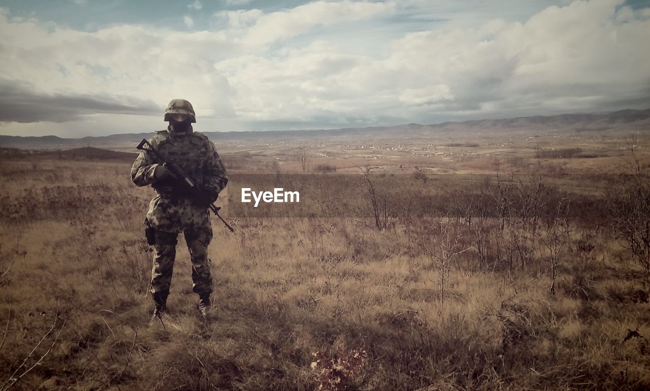 Full length of army soldier standing on field against cloudy sky