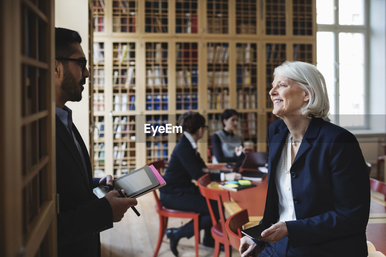 Happy senior professional discussing with coworker in board room at library