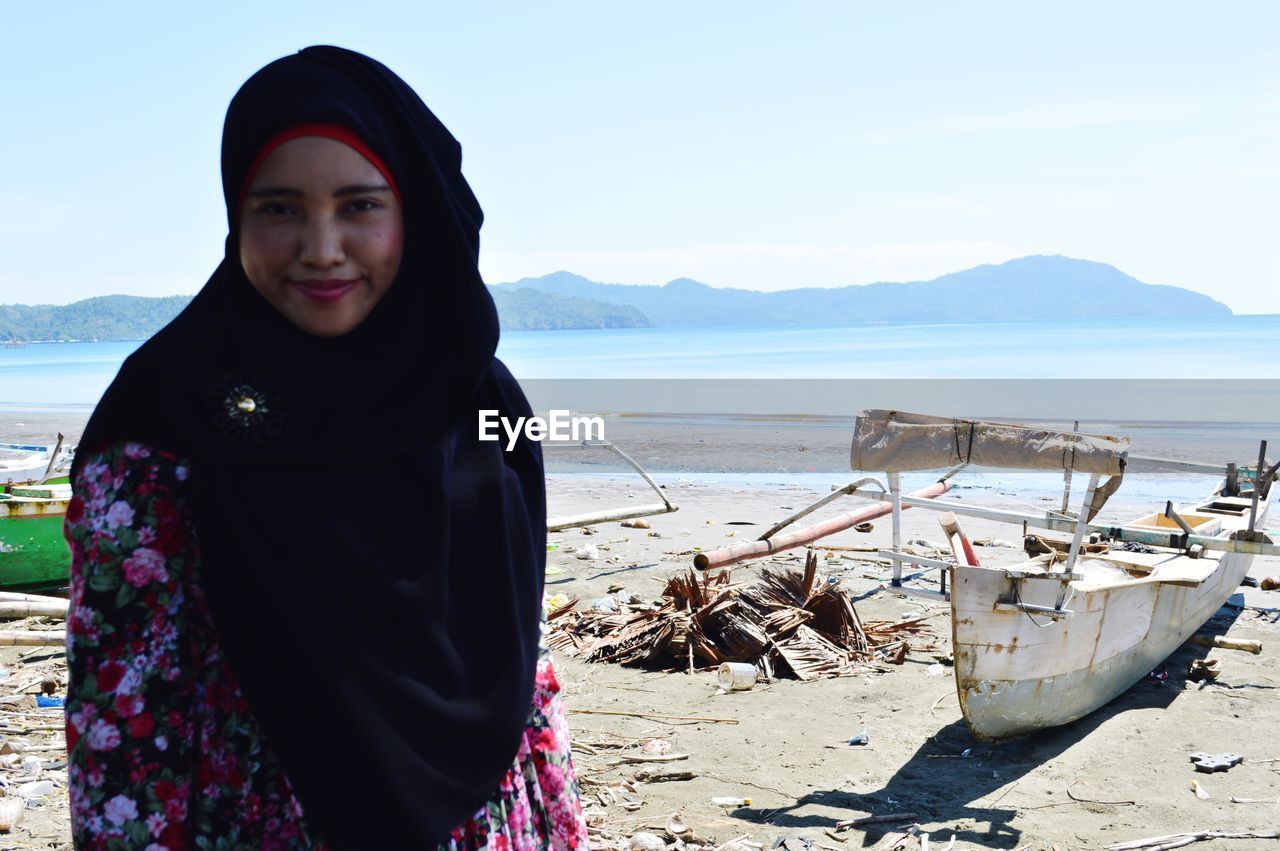 Portrait of smiling woman standing at beach against sky