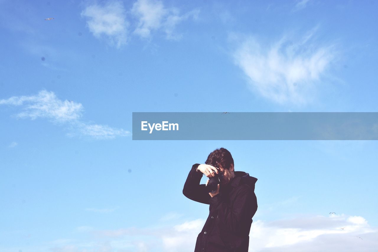 Low angle view of photographer against sky