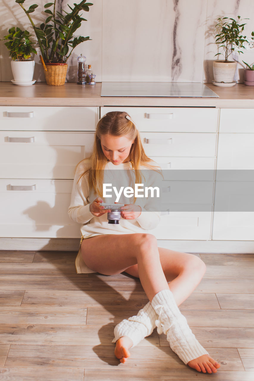 Full length of girl sitting on wooden floor at home