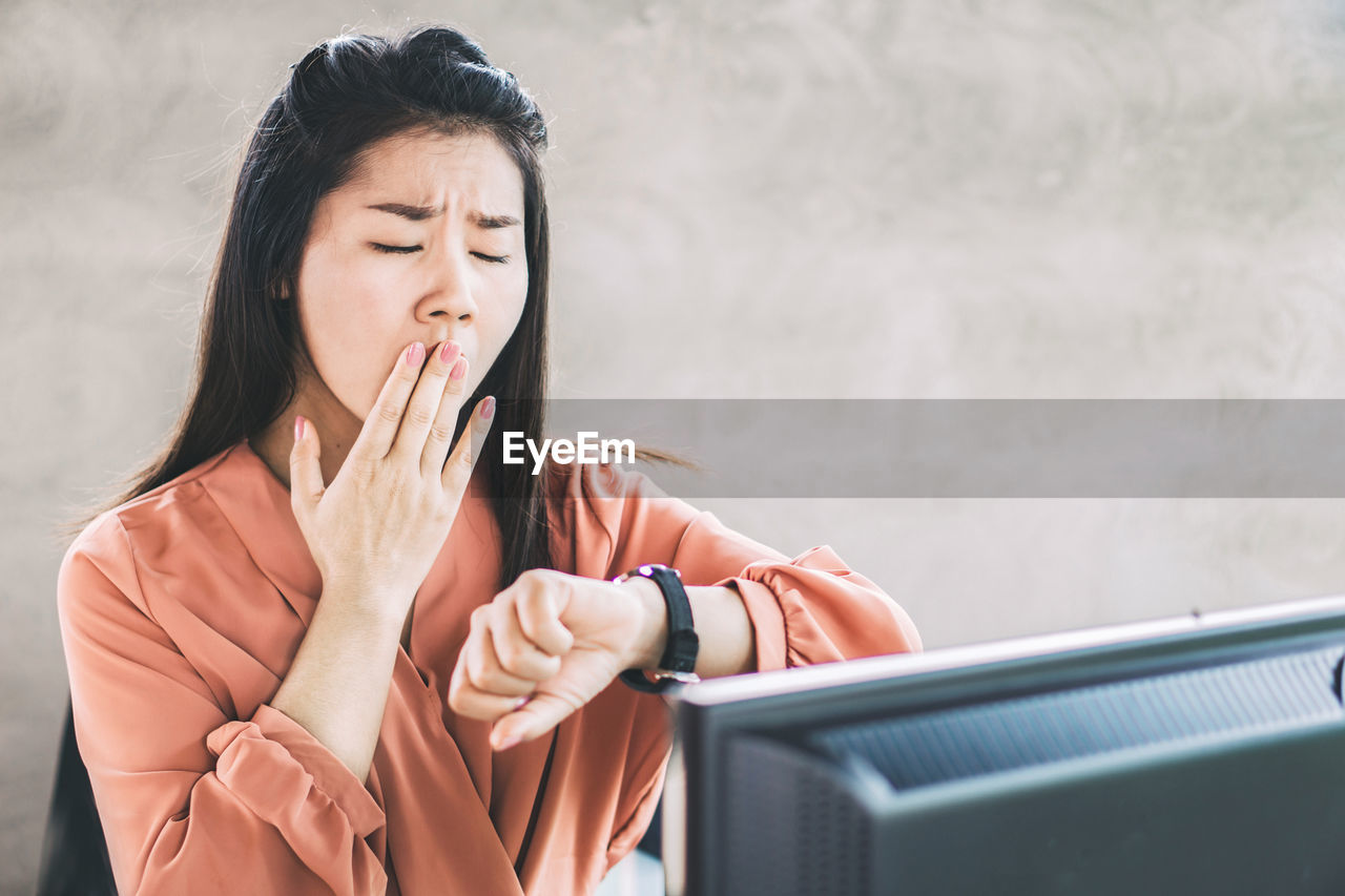 Woman yawning while watching time in office
