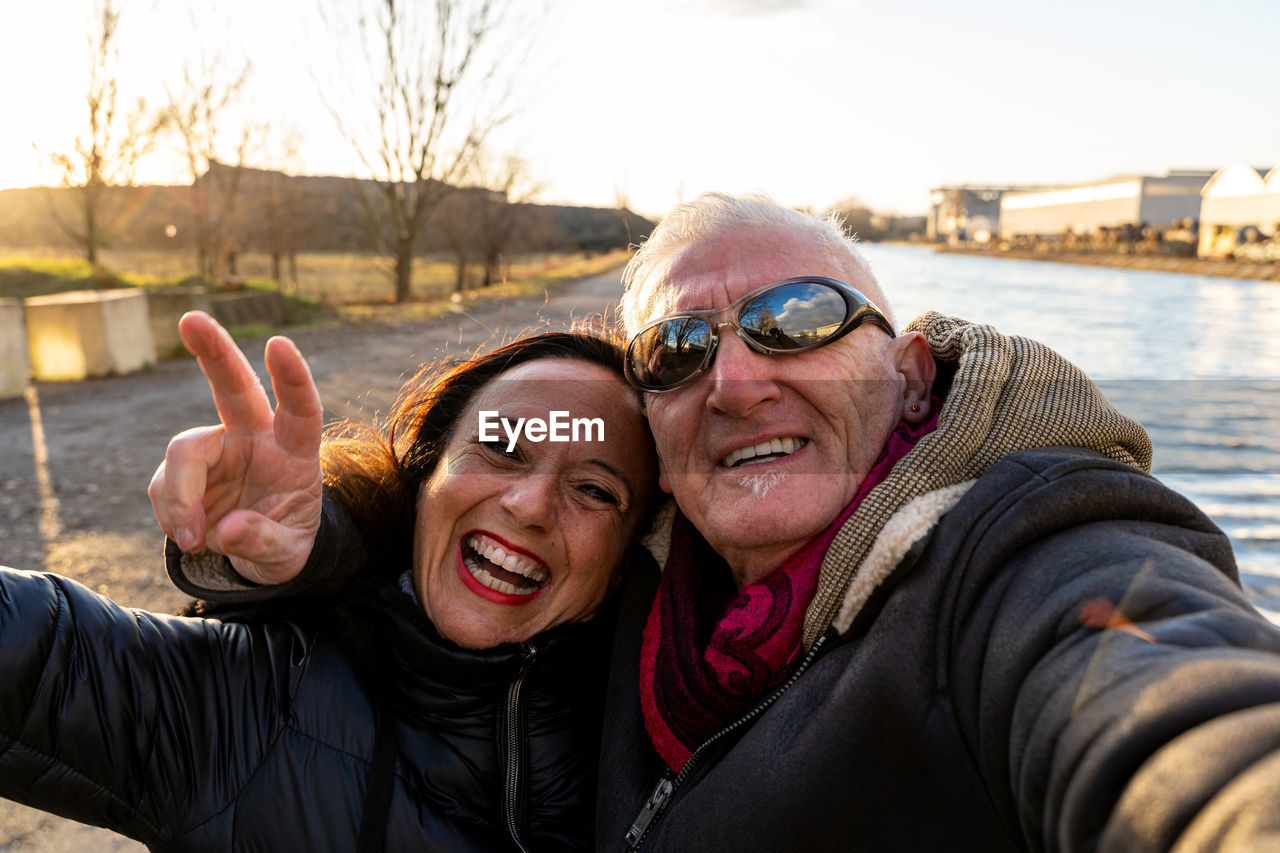 Middle aged couple wearing winter clothes taking a selfie on the river banks - people in recreation