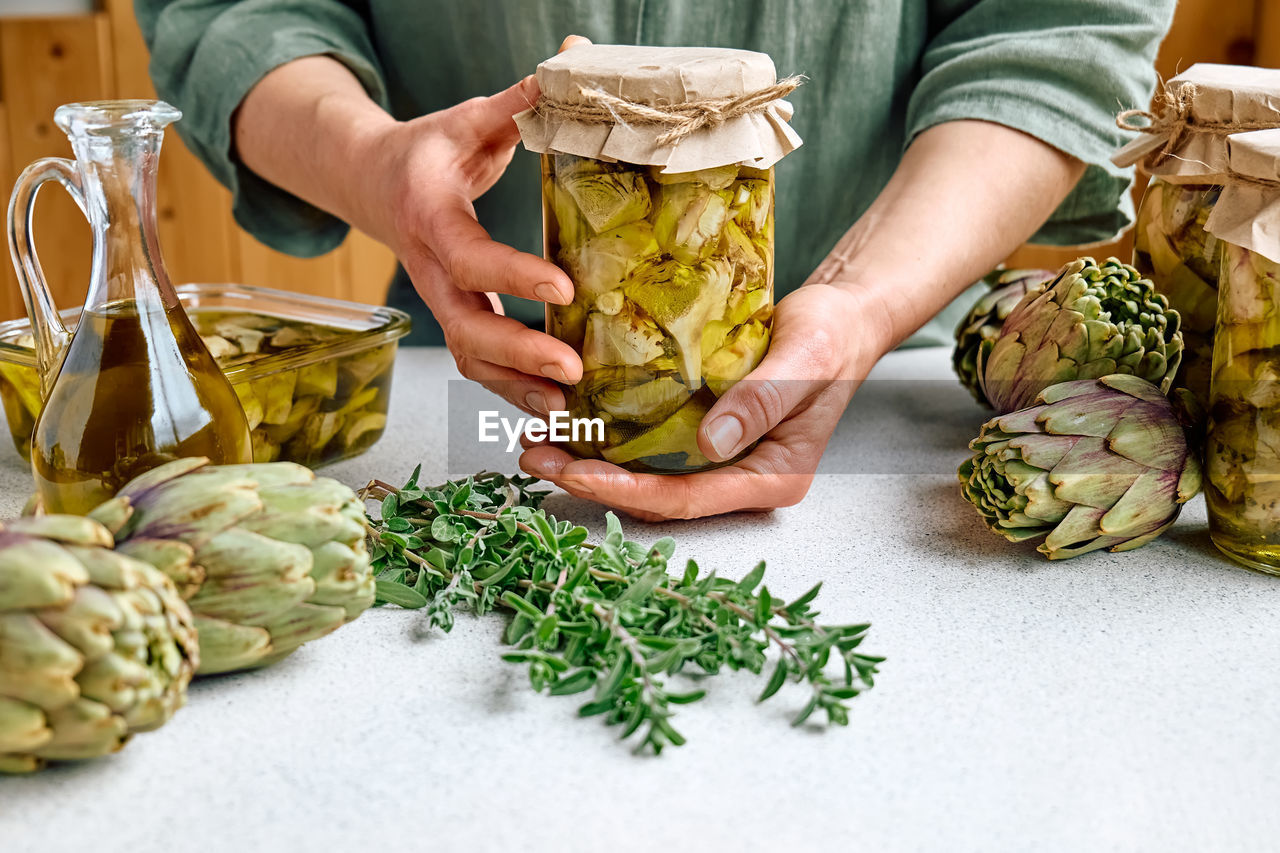 Artichoke hearts marinated with olive oil and herbs.woman holding glass jar with pickled artichokes.