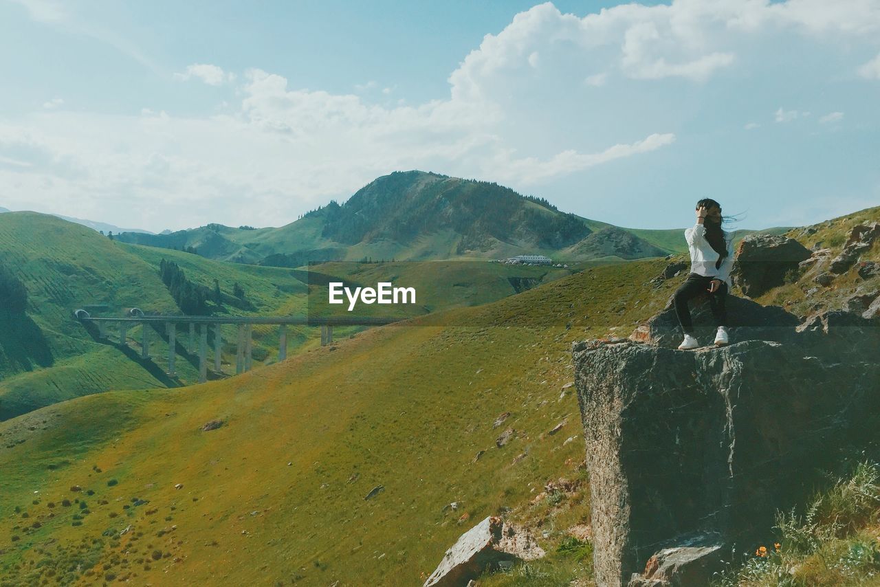 Full length of woman sitting on rock against mountain