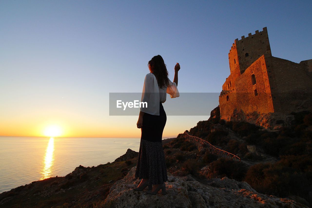 MAN STANDING ON ROCK AGAINST CLEAR SKY