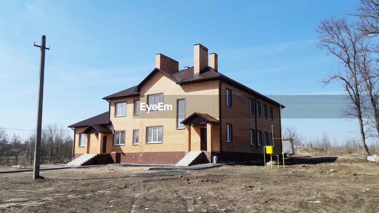 architecture, built structure, building exterior, building, house, sky, no people, day, nature, residential district, outdoors, low angle view, sunlight, blue, bare tree, field, window, tree, land, cloud - sky, housing development