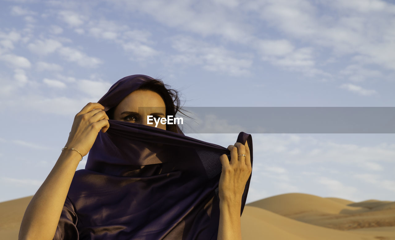 Woman wearing headscarf at desert against sky