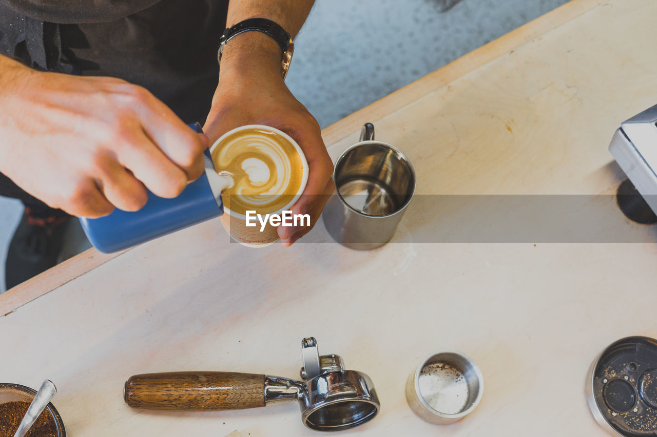 Cropped image of hand making froth art in espresso coffee at counter in cafe