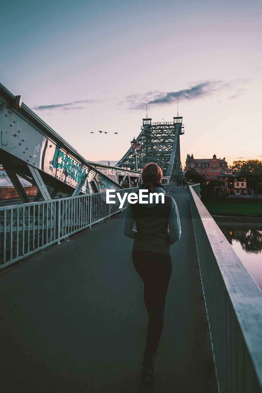 REAR VIEW OF MAN AND WOMAN STANDING AT SUSPENSION BRIDGE