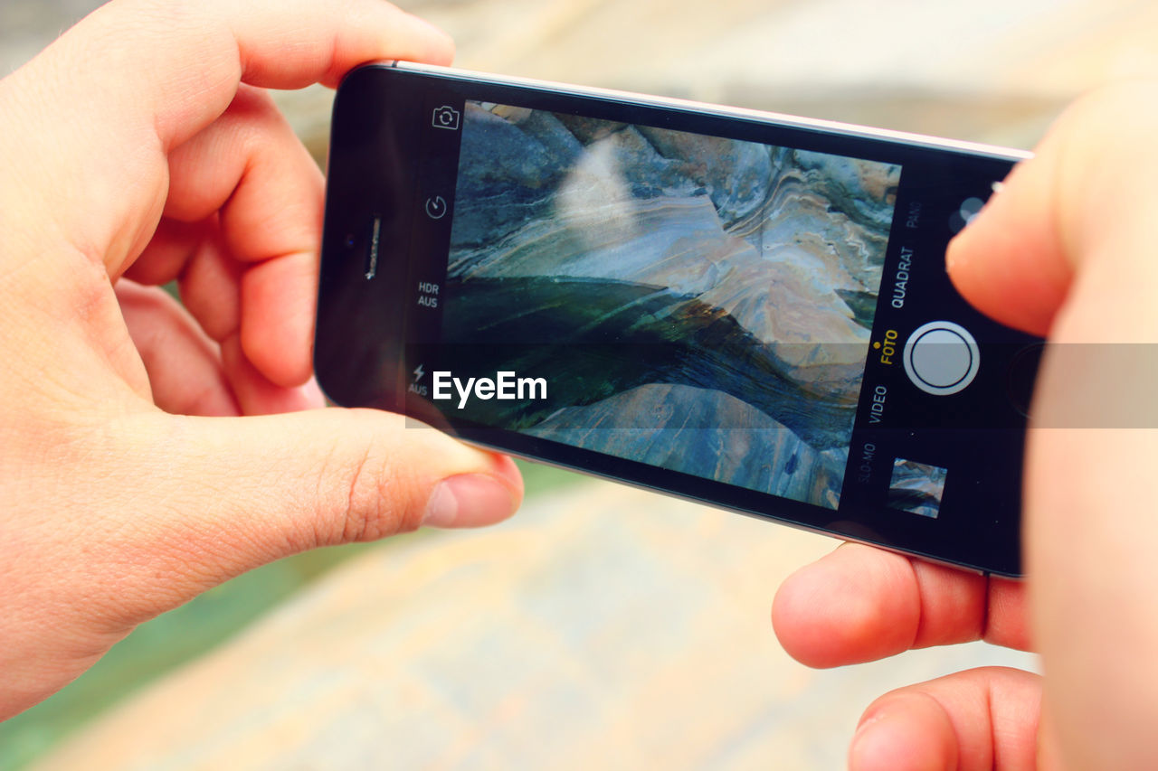 Close-up of cropped hand photographing rock formation through smart phone