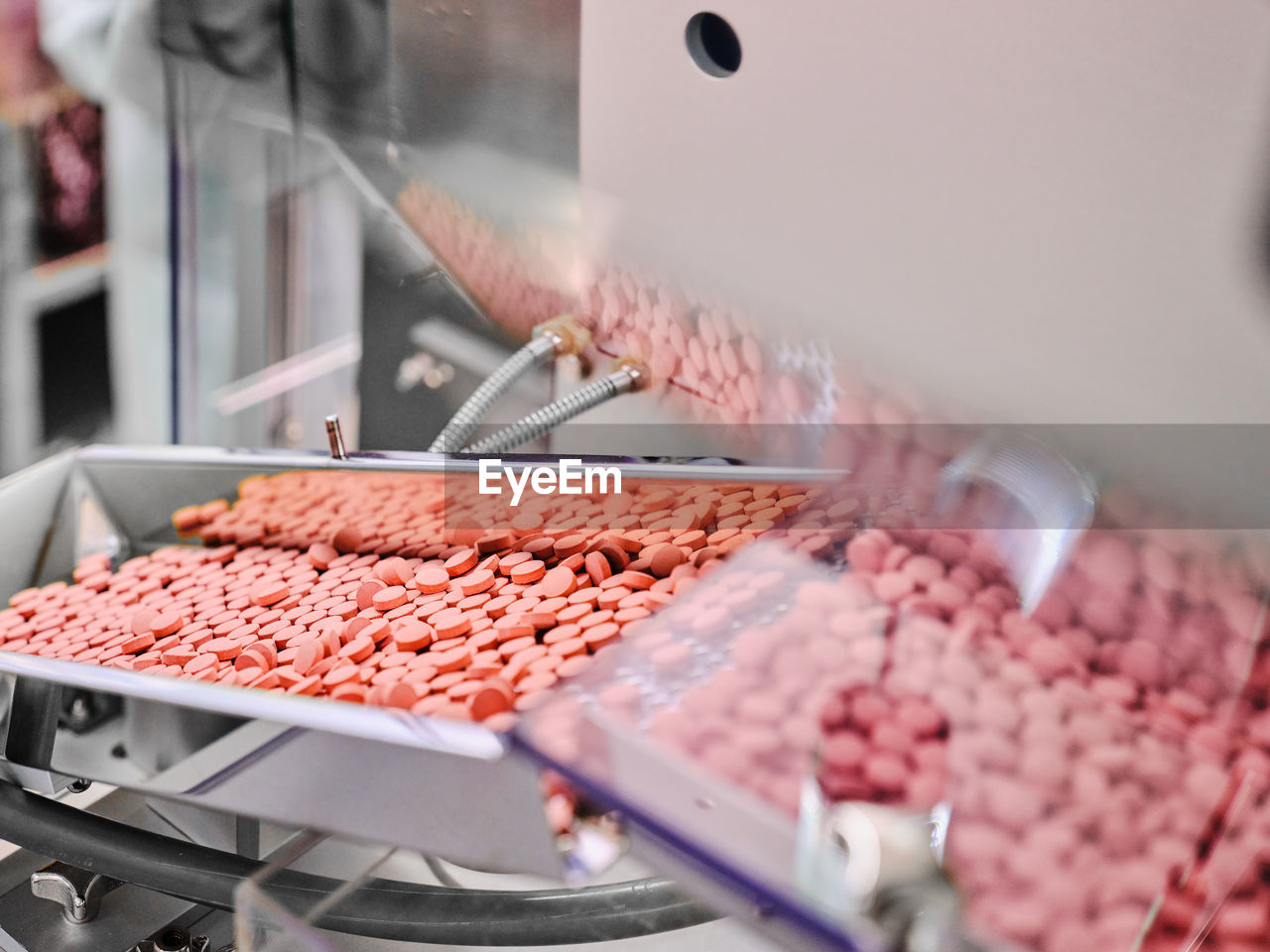 Contemporary pharmaceutical machine with piles of pink pills on conveyor placed in manufacturing laboratory