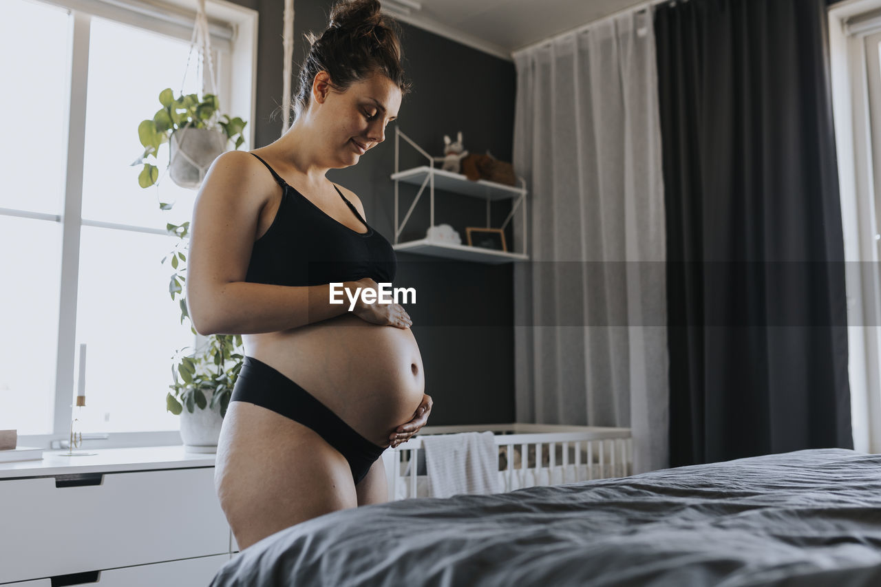 Pregnant woman massaging belly in bedroom