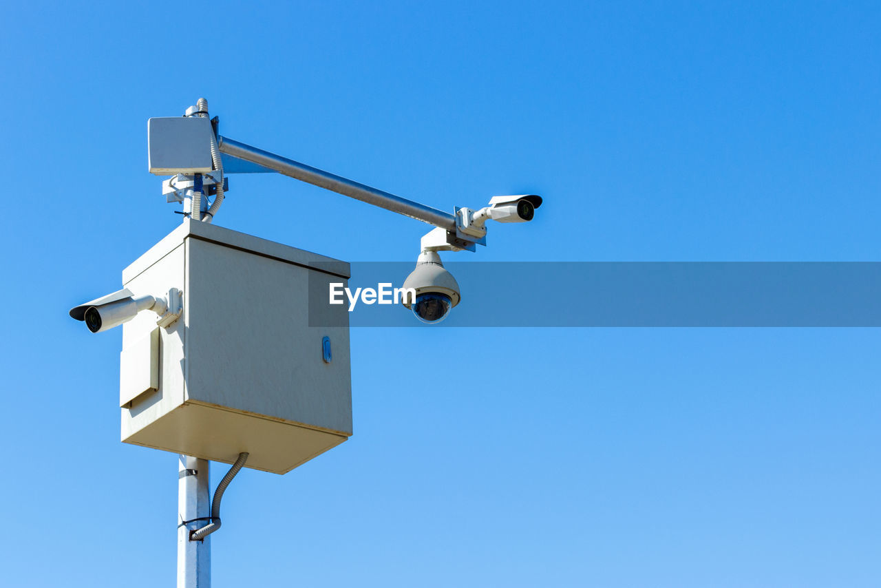 Low angle view of security camera against clear blue sky