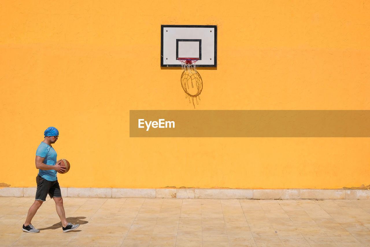 Side view of man playing basketball against yellow wall