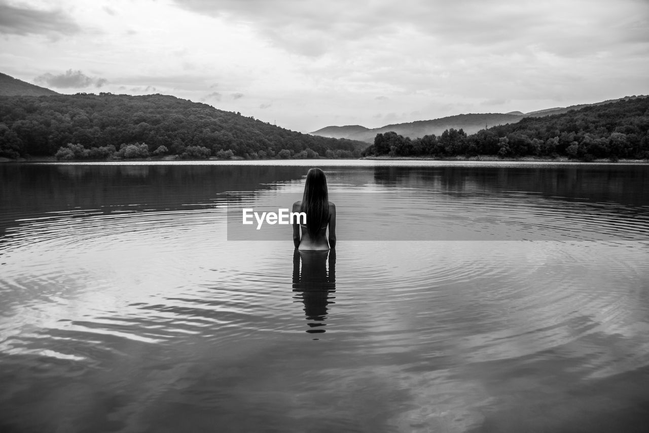 REAR VIEW OF MAN STANDING ON LAKE AGAINST SKY