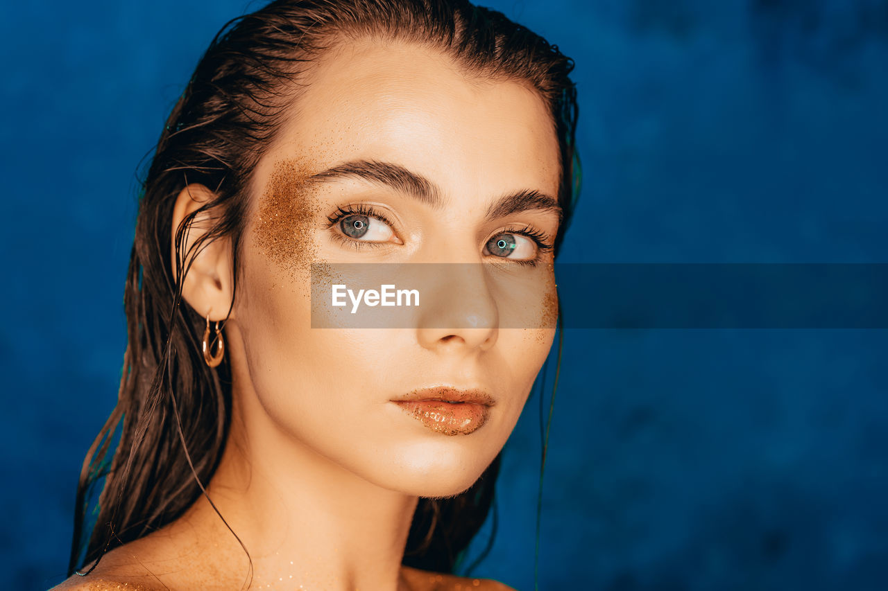 Close-up of woman with glitter on face against blue background