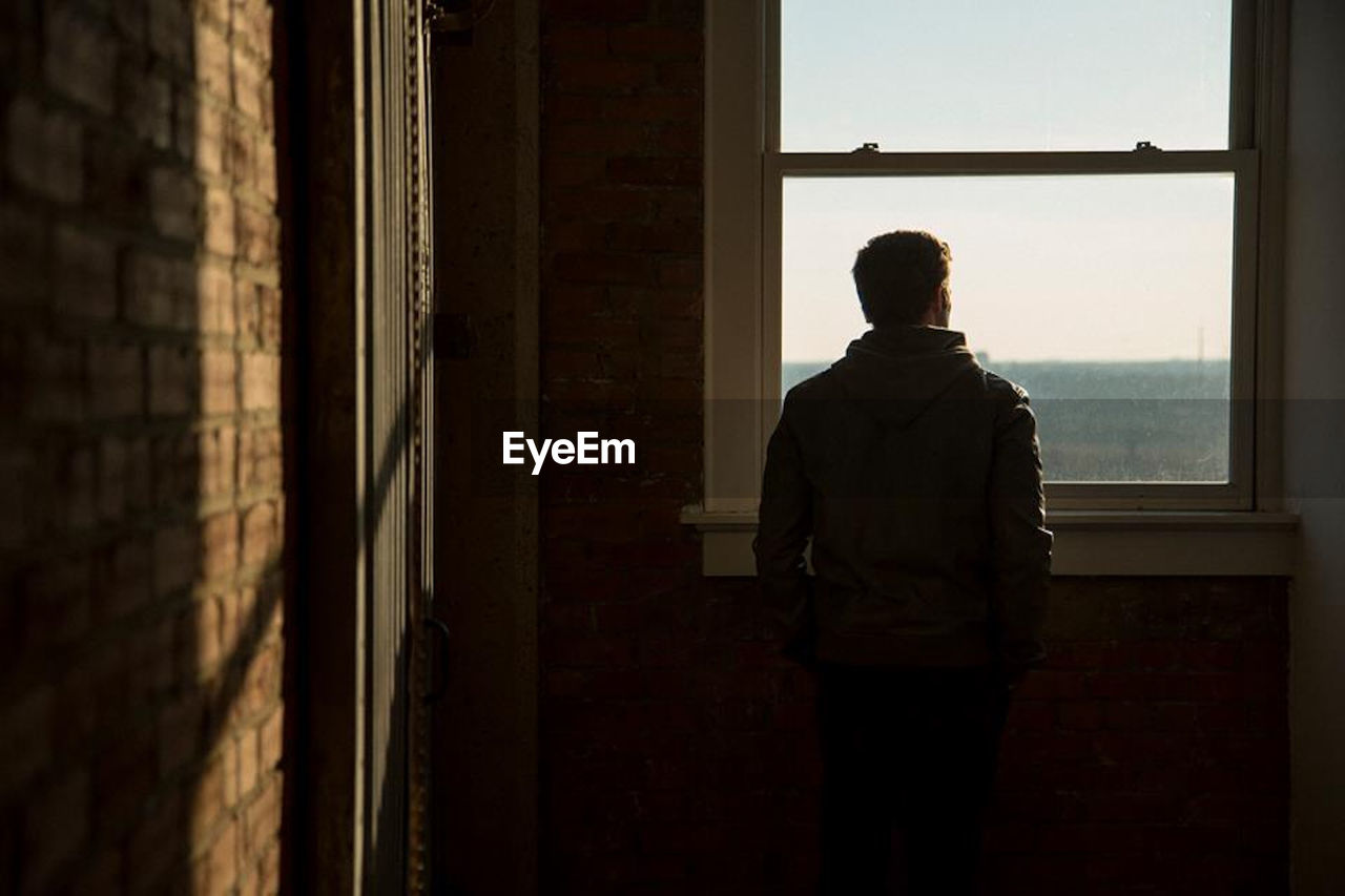 Rear view of man looking through window in building