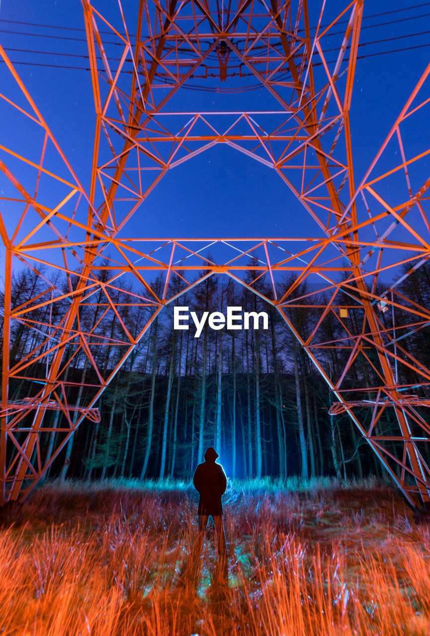 Man standing on field against electricity pylon at night