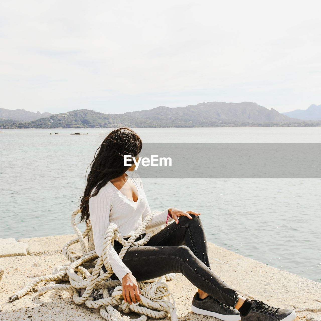 Woman sitting on mountain by lake against sky