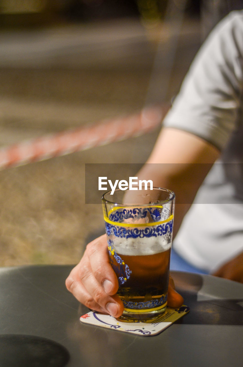 Midsection of man holding drink glass of cold beer