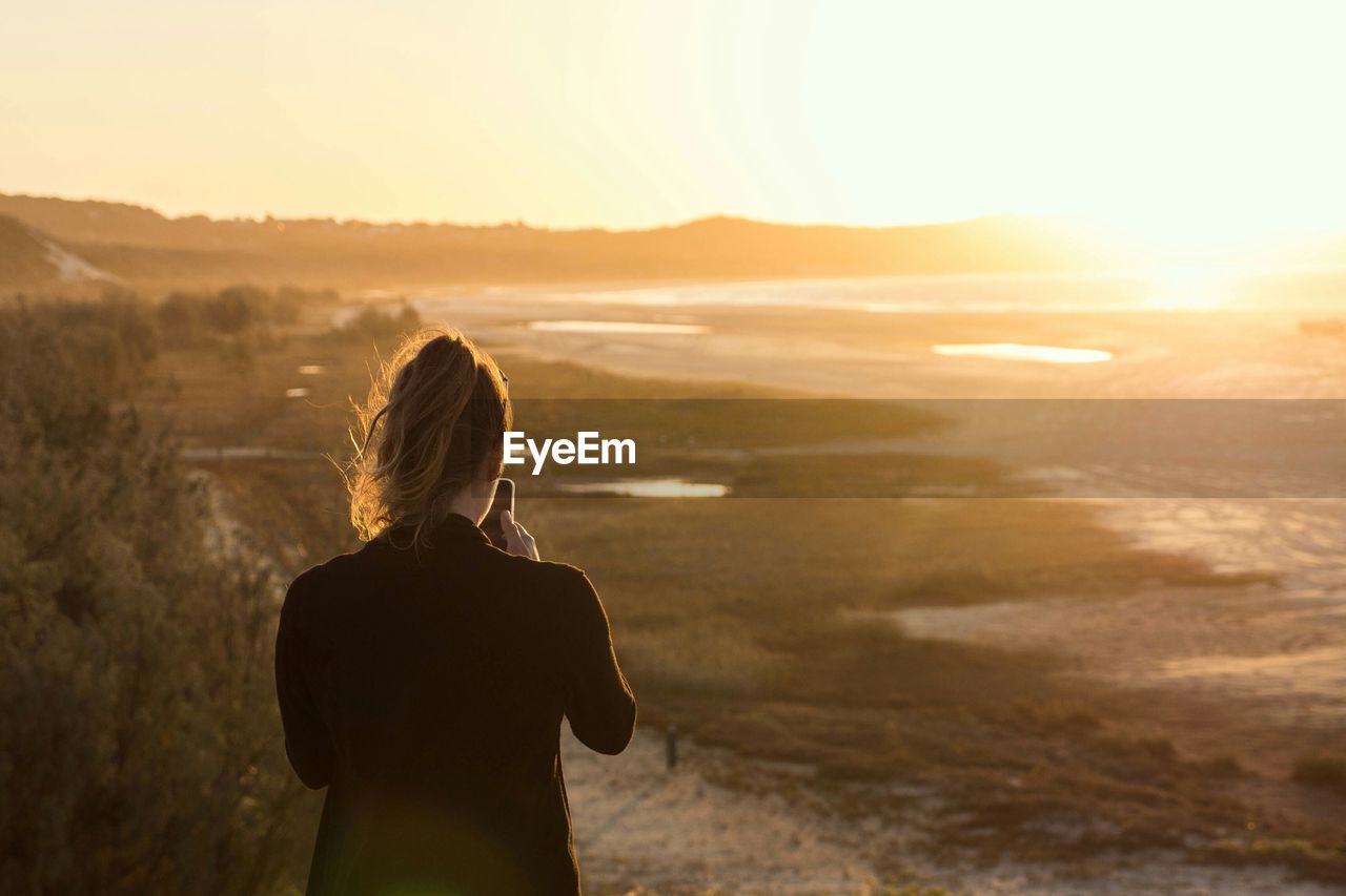 Rear view of woman using mobile phone on field during sunset