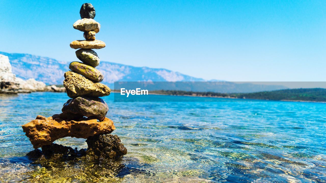 Stack of pebbles in sea against clear blue sky