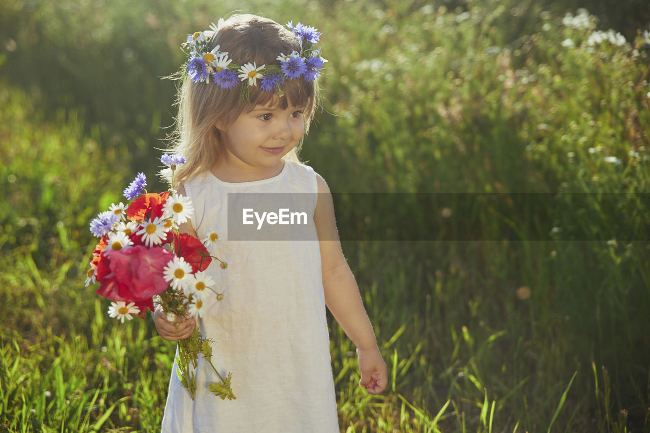 Charming child in linen dress walks in a field with flowers at sunset