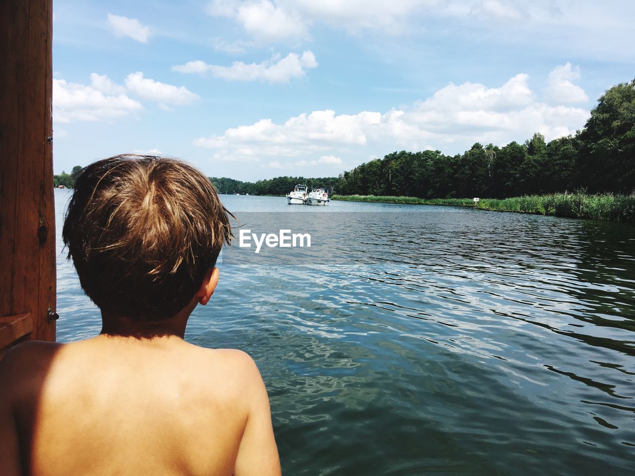 Rear view of shirtless boy looking at sea while standing against sky