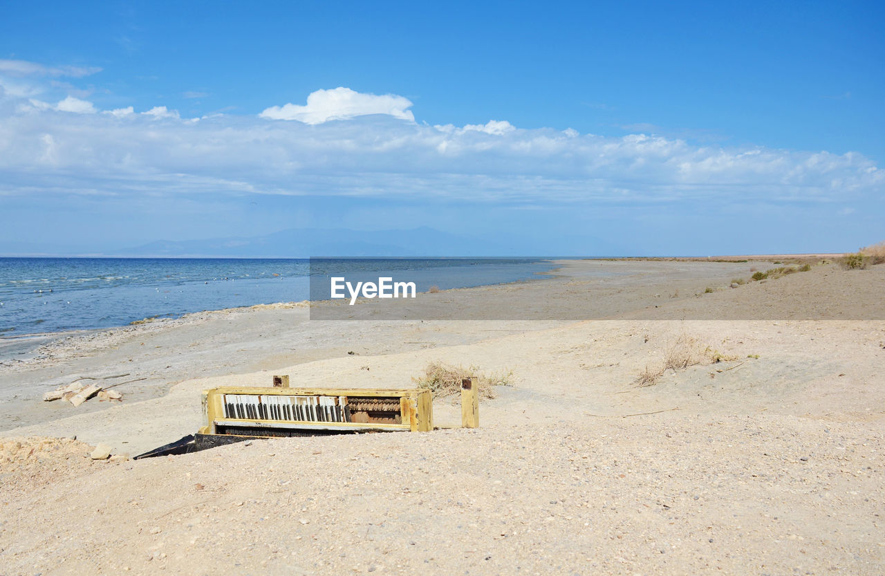 Abandoned piano at beach against sky