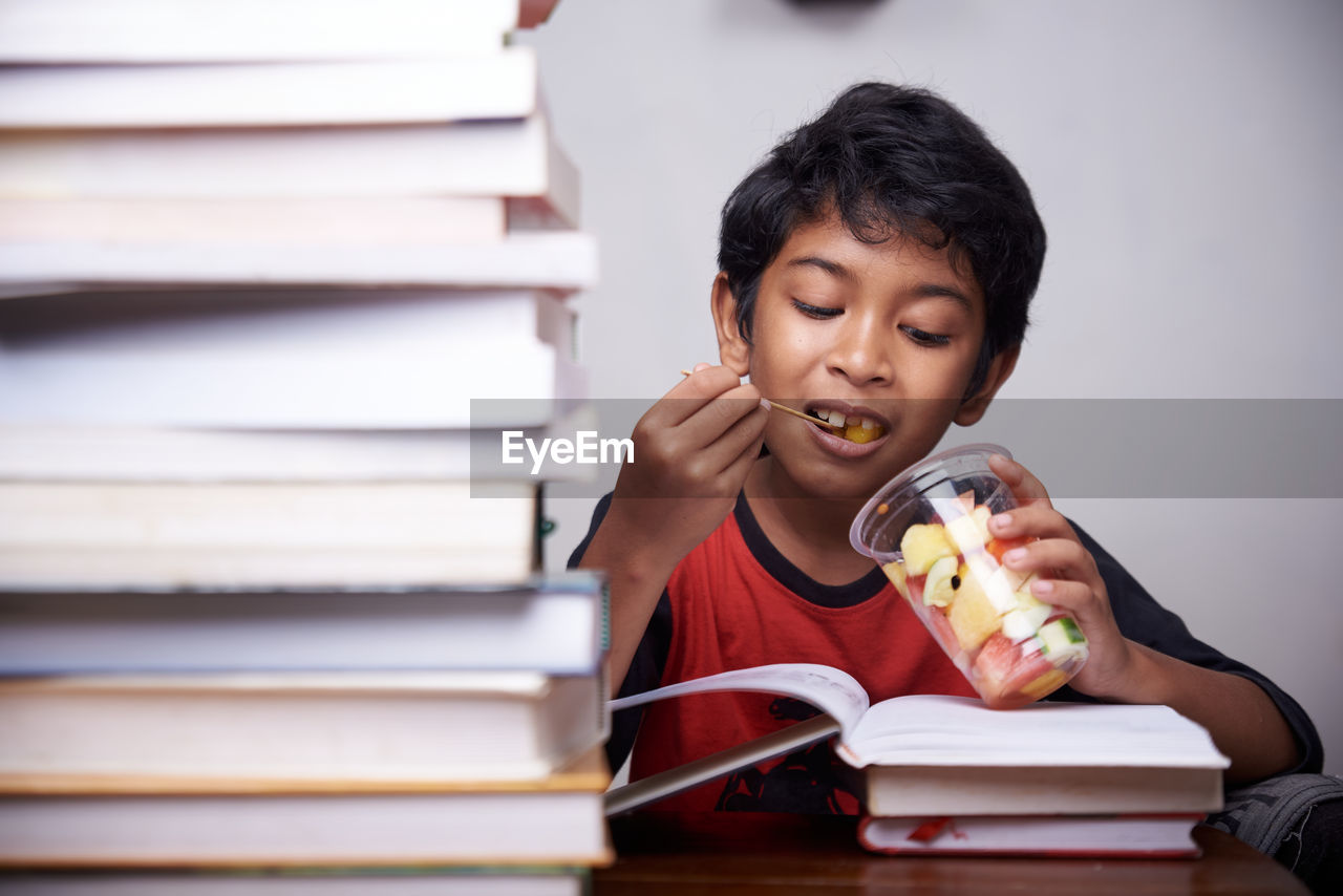 Little boy eating mixed fruit after study at home